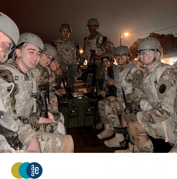 New York City endodontist Doctor Austin Whitmore with a group of people in military uniforms and helmets, smiling while seated around equipment boxes at night.