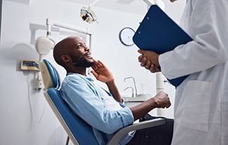 a dental patient holding his mouth and speaking with a dentist