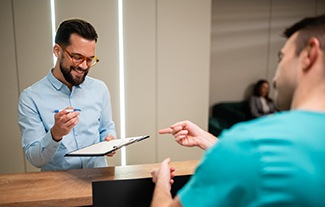 a man filling out forms on a clipboard while a man in scrubs points at the forms