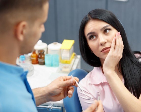 Woman holding her cheek in pain while talking to emergency dentist