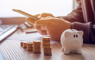 Person using a calculator at their desk next to a piggy bank and coin stacks