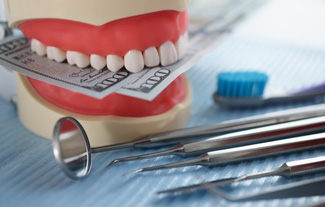 Dental model biting down on paper money next to dental tools