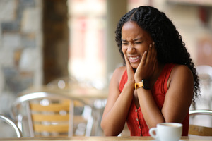 Woman sitting at table in café dealing with tooth pain