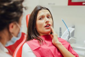 Woman in dentist's chair holding her hand to her jaw